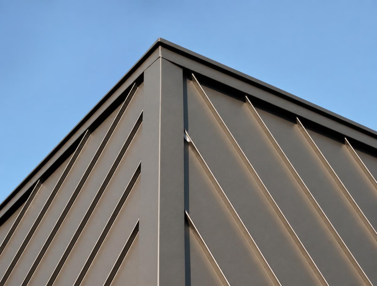 Close-up of a bronze standing seam metal roof ridge against a blue sky